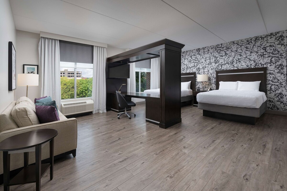A hotel room with a bed, a desk, a chair, a sofa, and a view of the outdoors.
