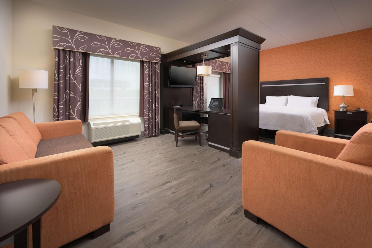 A hotel room with a bed, a desk, a chair, and two armchairs.