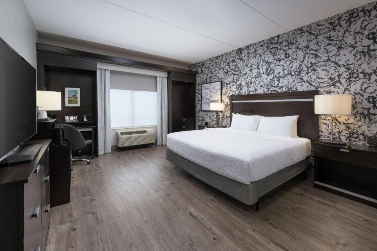 A hotel room with a large bed, a desk with a chair, a TV, and a window with curtains.