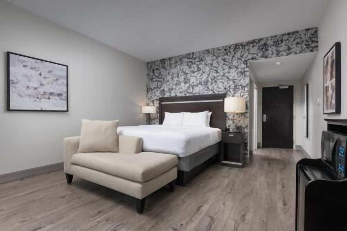 A hotel room with a bed, a sofa, a desk, and a door.