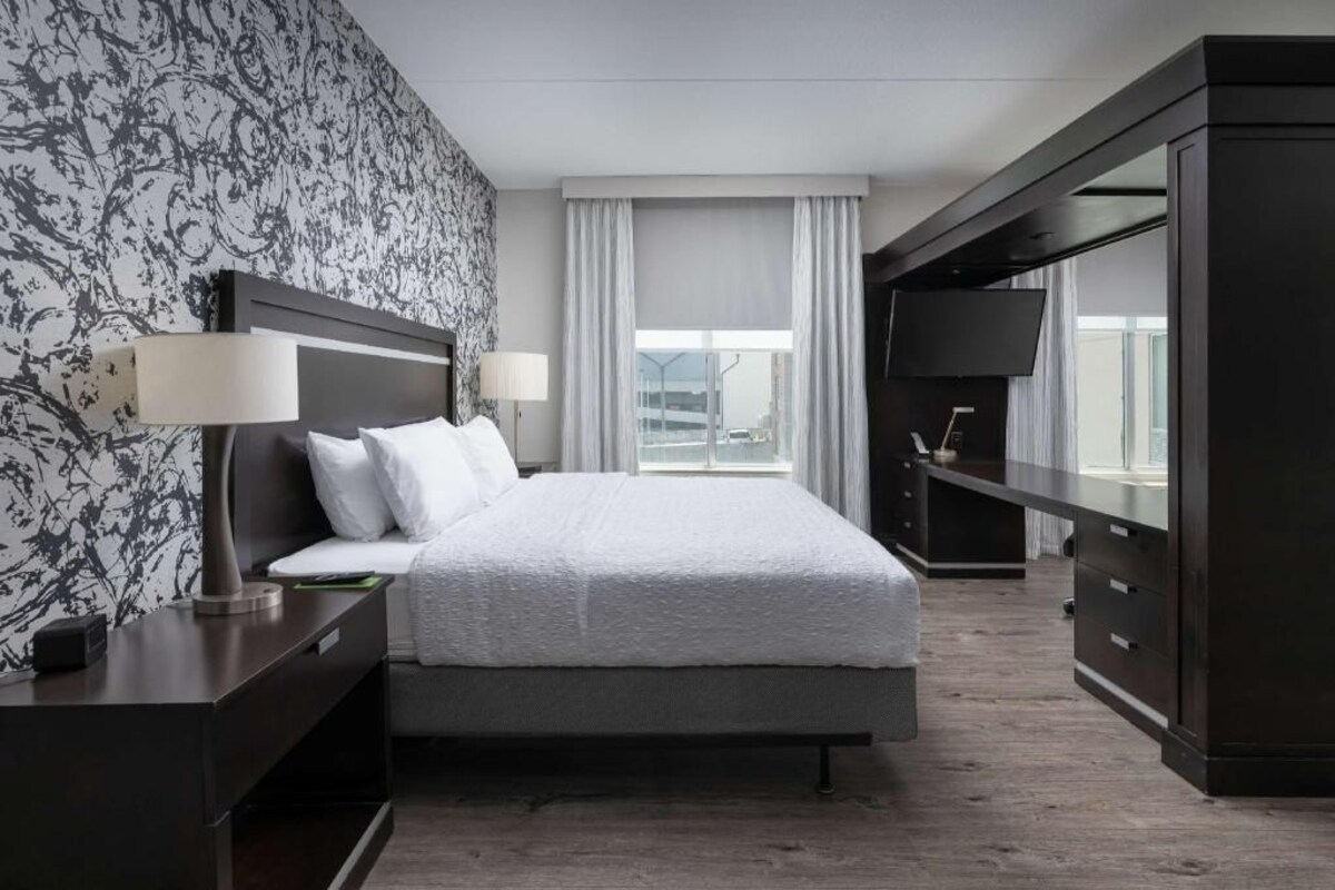 A hotel room with a bed, bedside tables, a TV, and a window with curtains.