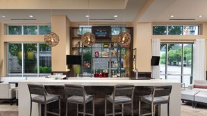 A modern bar area with a long counter, four bar stools, and hanging pendant lights. - Hampton Inn & Suites Chattanooga/Downtown (Chattanooga)