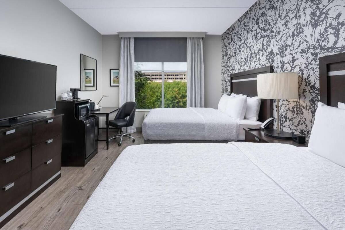 Une chambre d’hôtel avec deux lits, un bureau, une télévision et une fenêtre donnant sur des immeubles et des arbres.