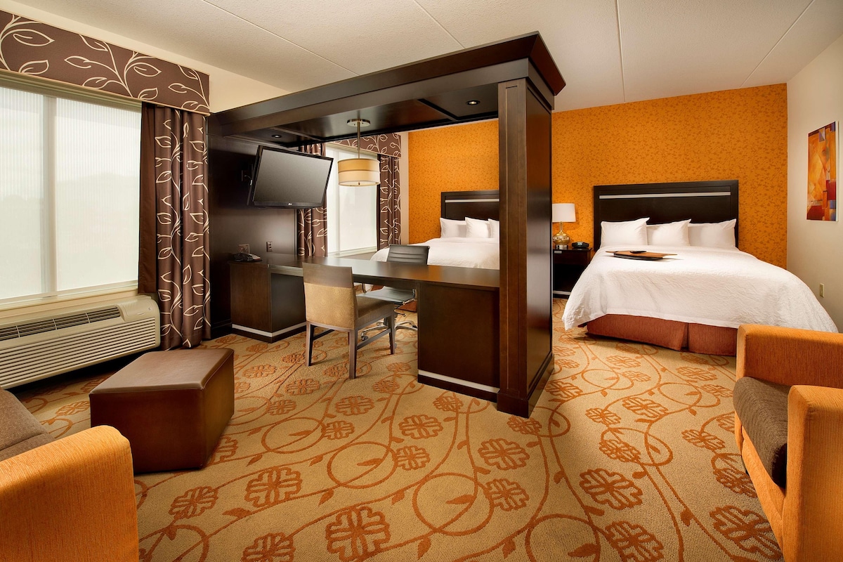 A hotel room with a bed, a desk, a chair, a television, and a window with curtains.
