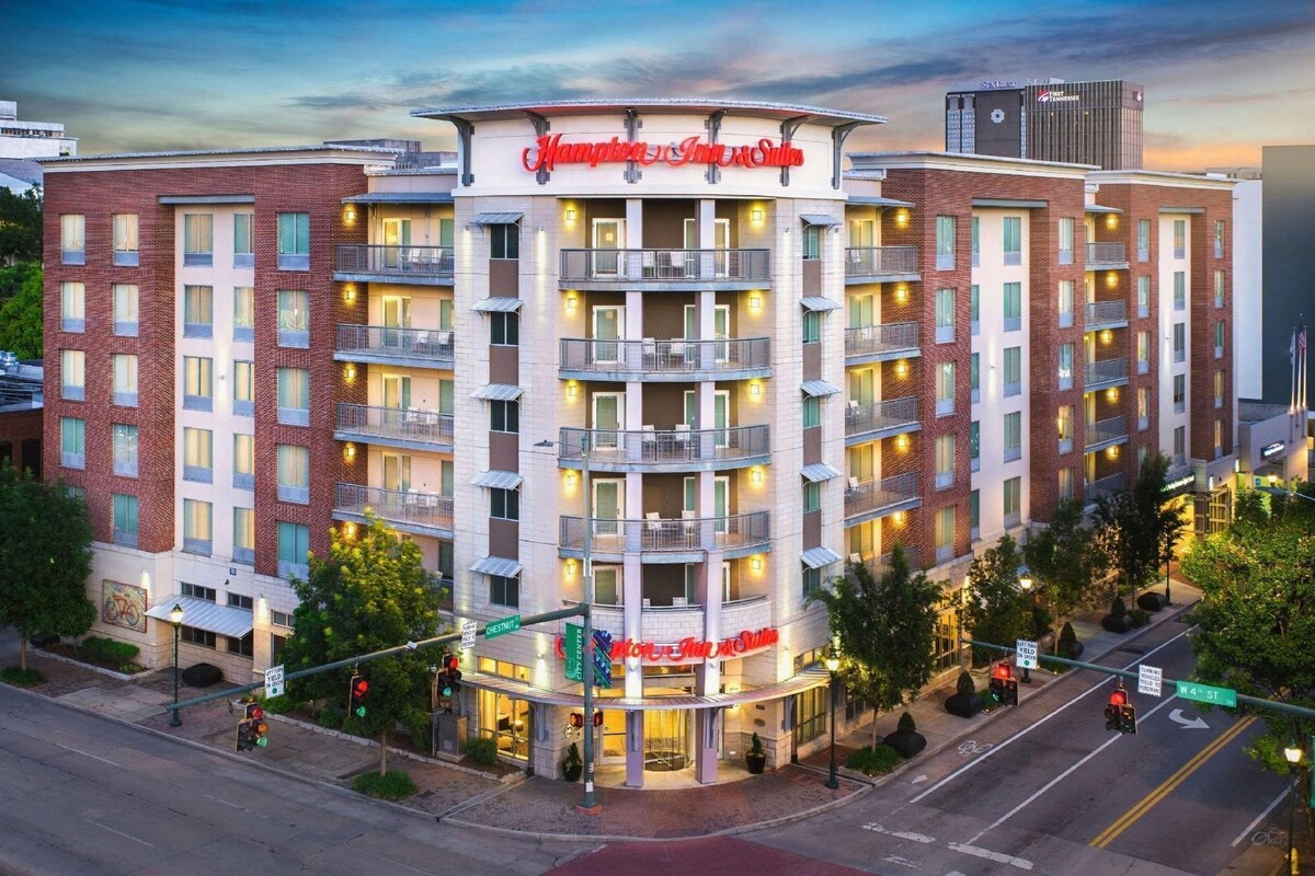 A multi-story hotel with a prominent Hampton Inn & Suites sign, multiple balconies, and a ground-level entrance.