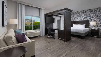 A modern hotel room with a bed, a desk, a chair, a sofa, and a TV.