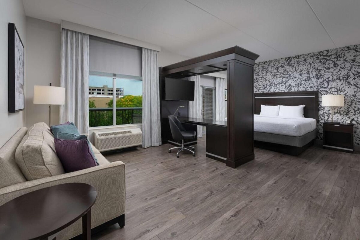 A hotel room with a bed, a desk, a chair, a TV, and a window with curtains.