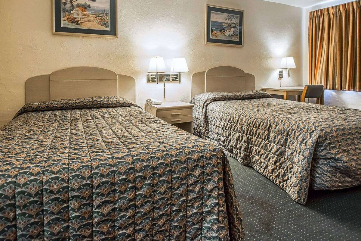 Quarto de hotel com duas camas, uma escrivaninha e duas luminárias.