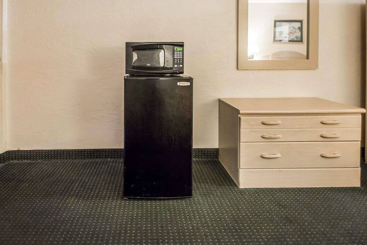 Uma cozinha compacta com micro-ondas, um refrigerador pequeno e um armário bege com gavetas.