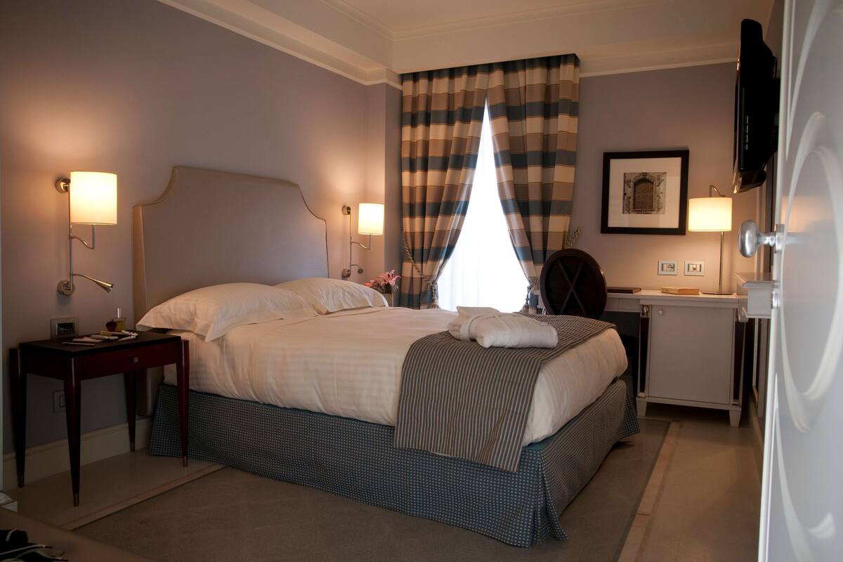 A neatly arranged hotel room with a large bed, two bedside tables, a small desk, and a television.