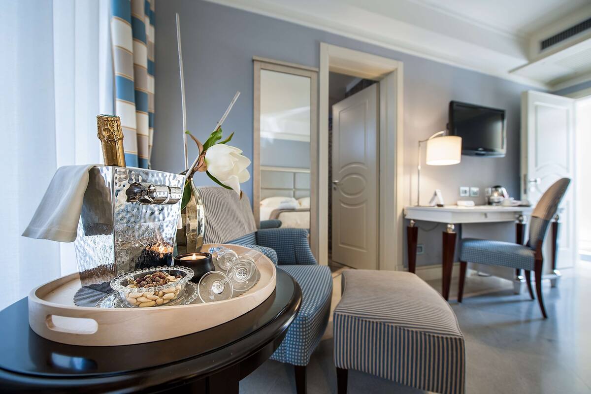 A hotel room with a dining area featuring a table with a decorative centerpiece, a sofa, a chair, and a television mounted on the wall.