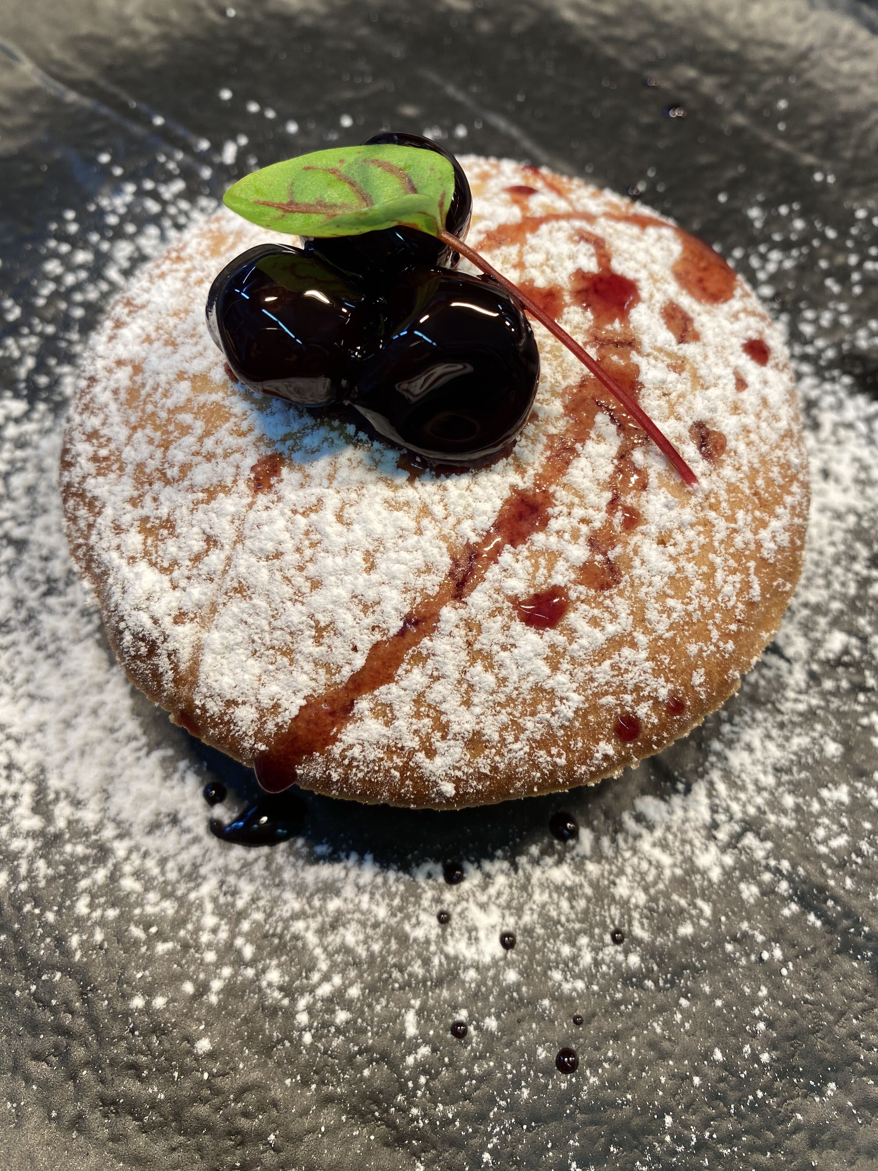 A dessert with powdered sugar, cherries, and a leaf garnish on a plate.