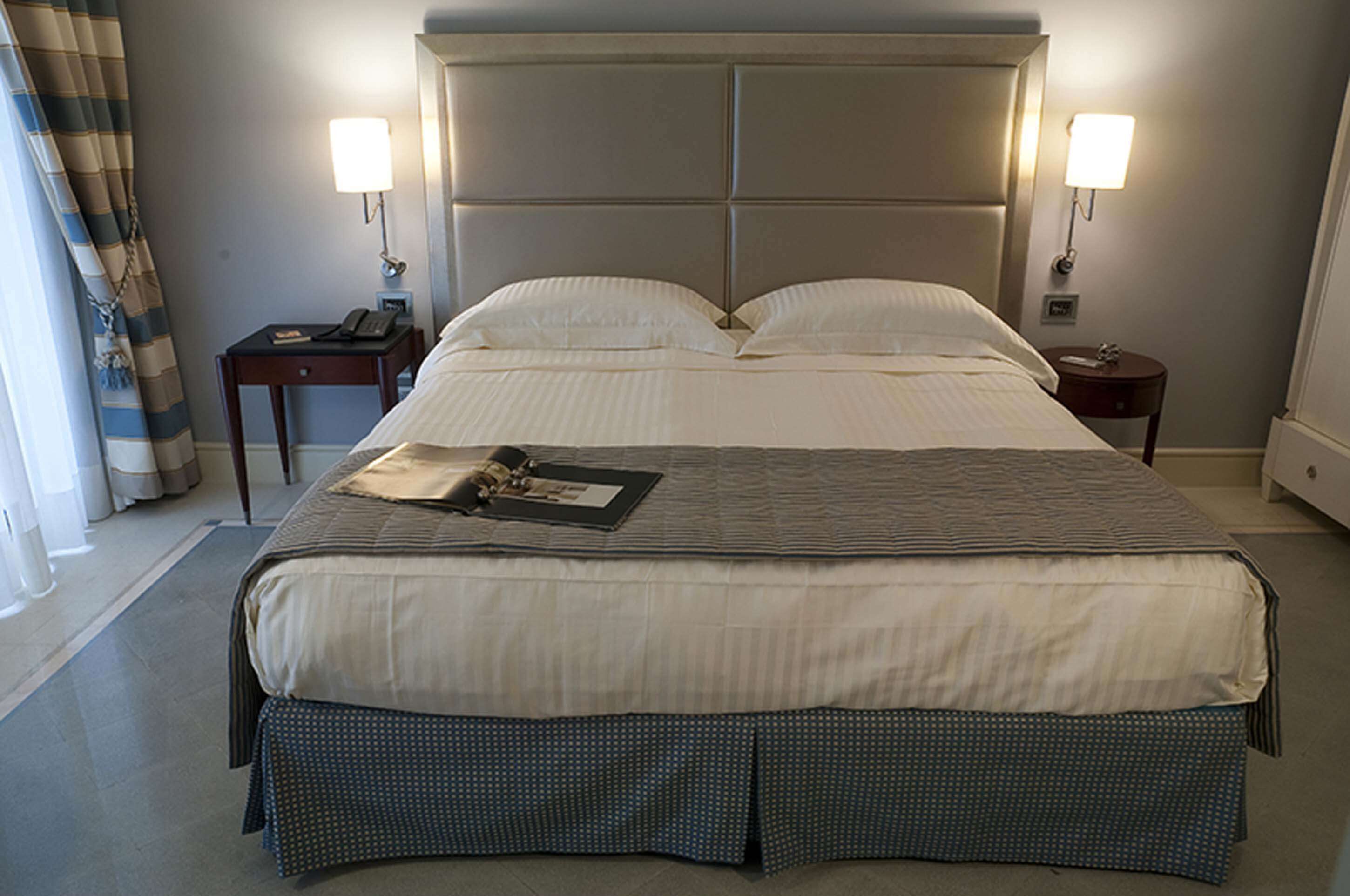 A hotel room with a large bed, two bedside tables, a lamp on each table, and a curtain on the window.