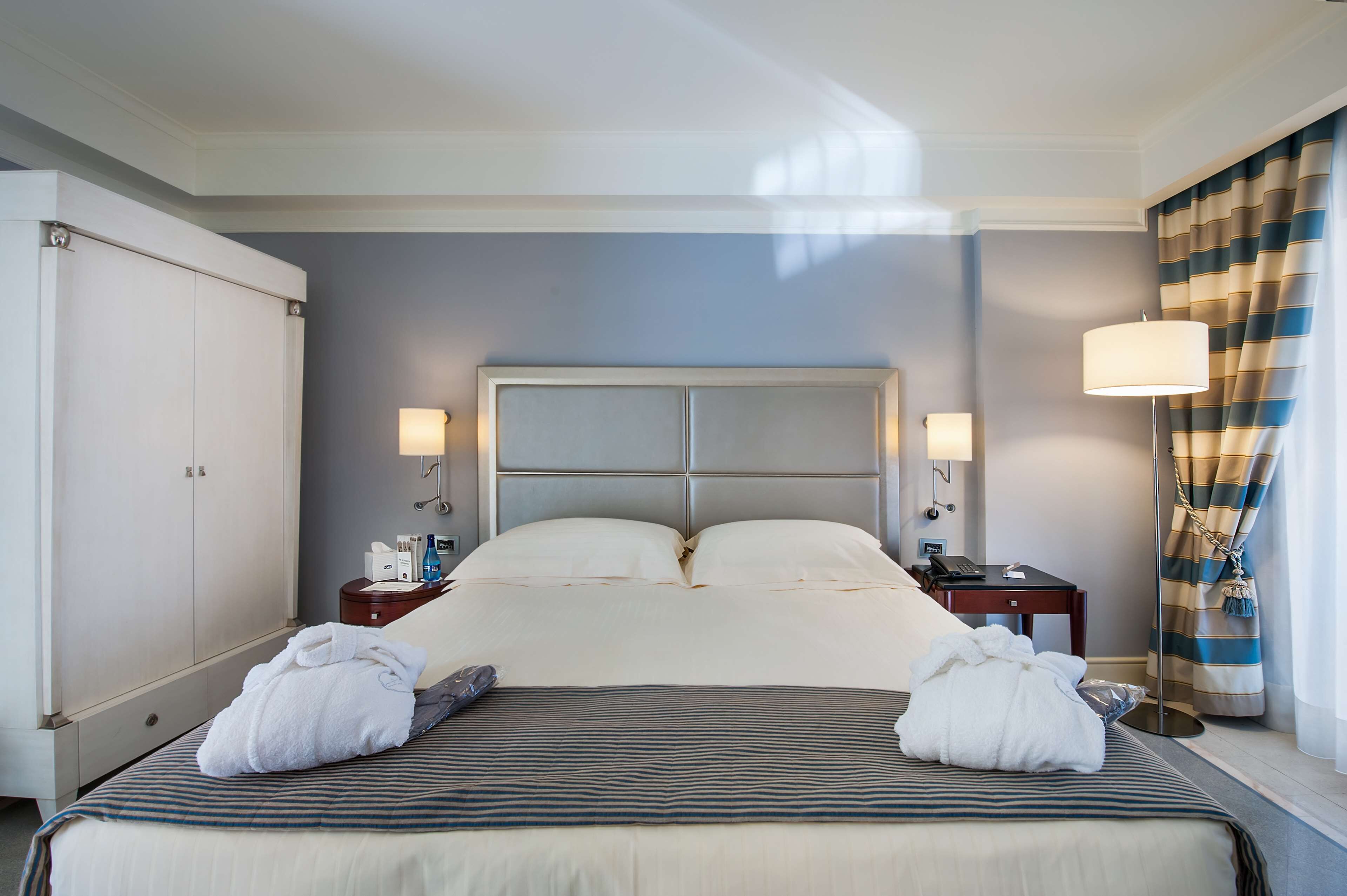 Una habitación de hotel con una cama grande, dos mesitas de noche y una lámpara.