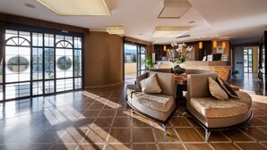 A spacious living area with a curved sofa set, a dining table, and a large window with a view of the outdoors.