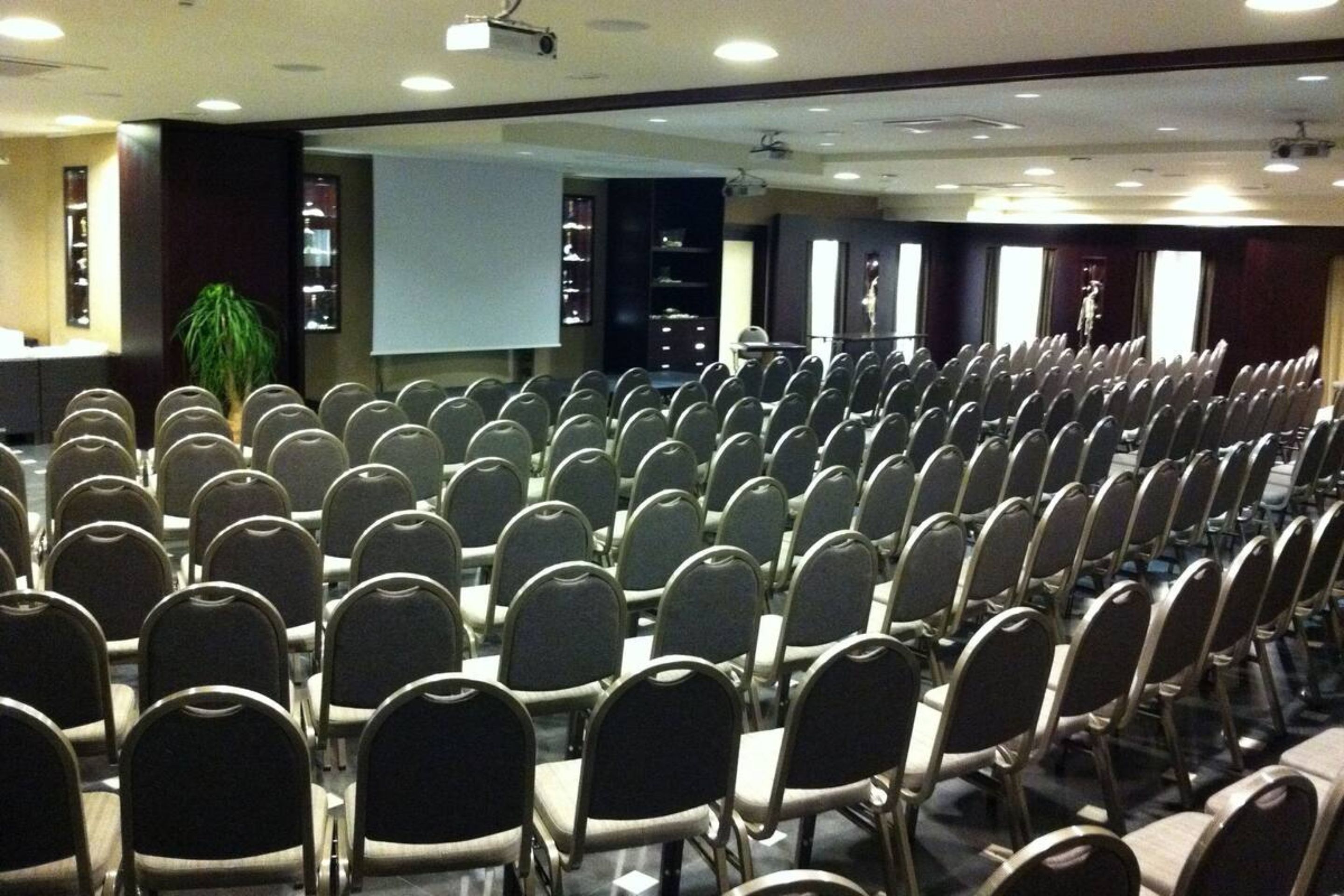 Ein Konferenzraum mit Reihen von Stühlen, einer Projektionsleinwand und einer Bühne.