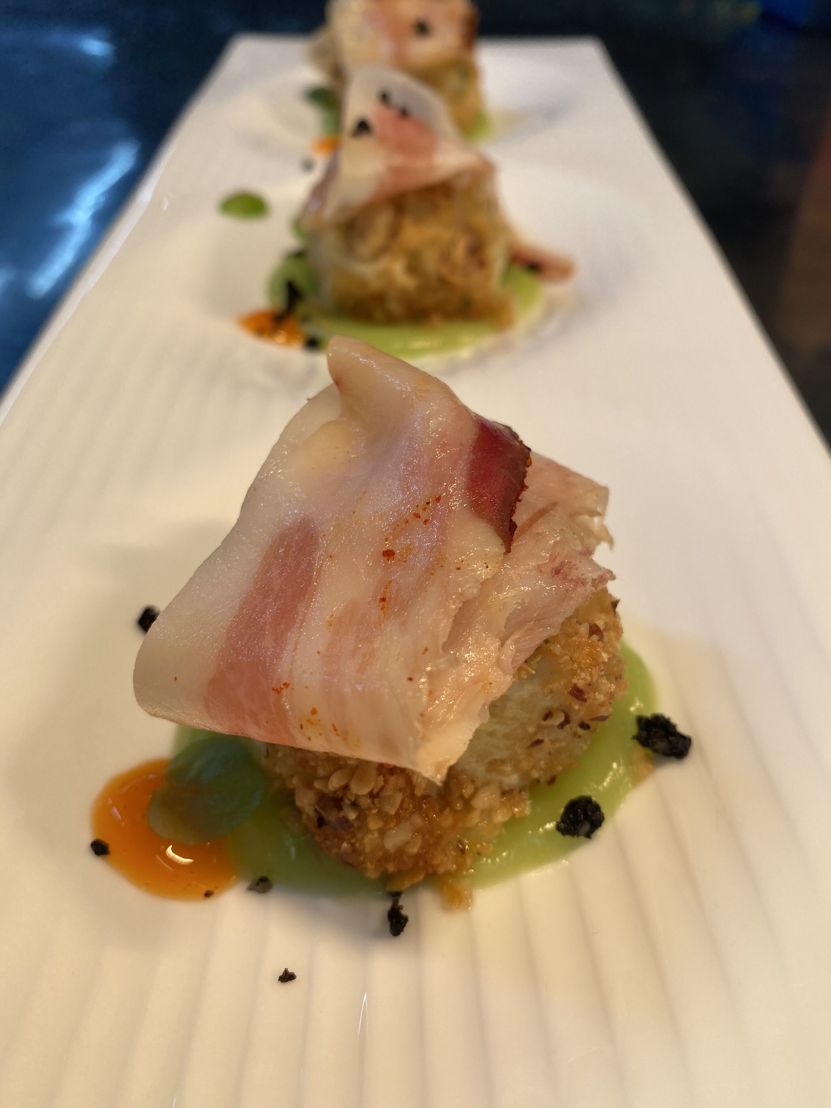 A dish with a crispy base, topped with a translucent, pinkish layer, and a green sauce.