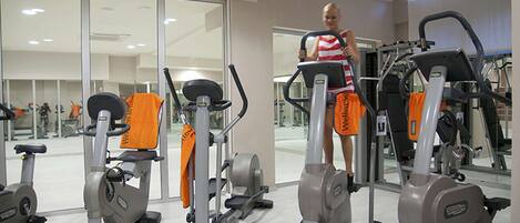 A gym with various exercise machines, including treadmills and elliptical trainers, arranged in a spacious room with large windows.