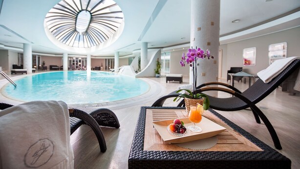 A poolside area with lounge chairs, a tray with fruit and a drink, and a large circular skylight.
