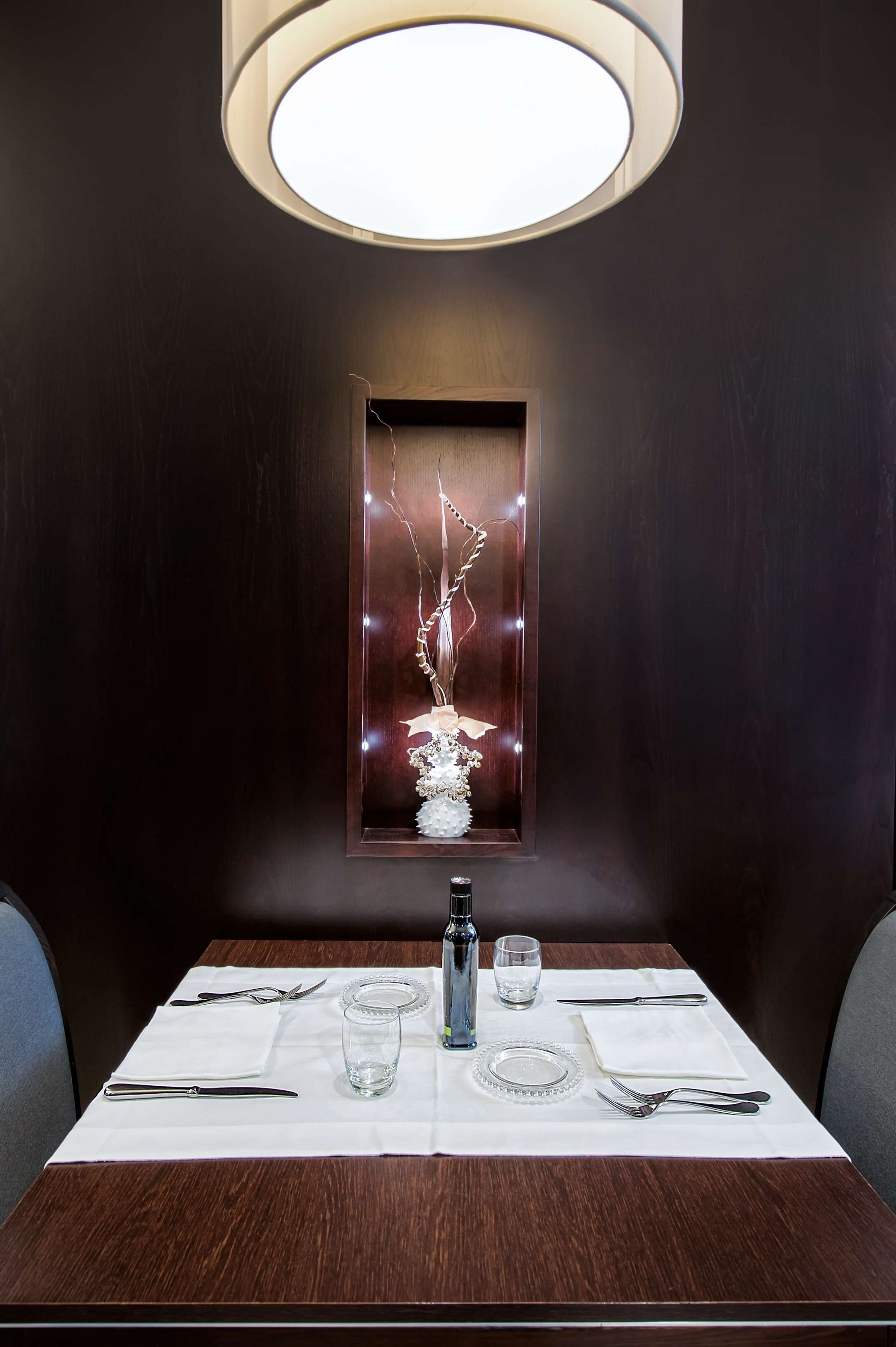 A dining table set with cutlery and glasses, a vase with flowers, and a wall-mounted light fixture.