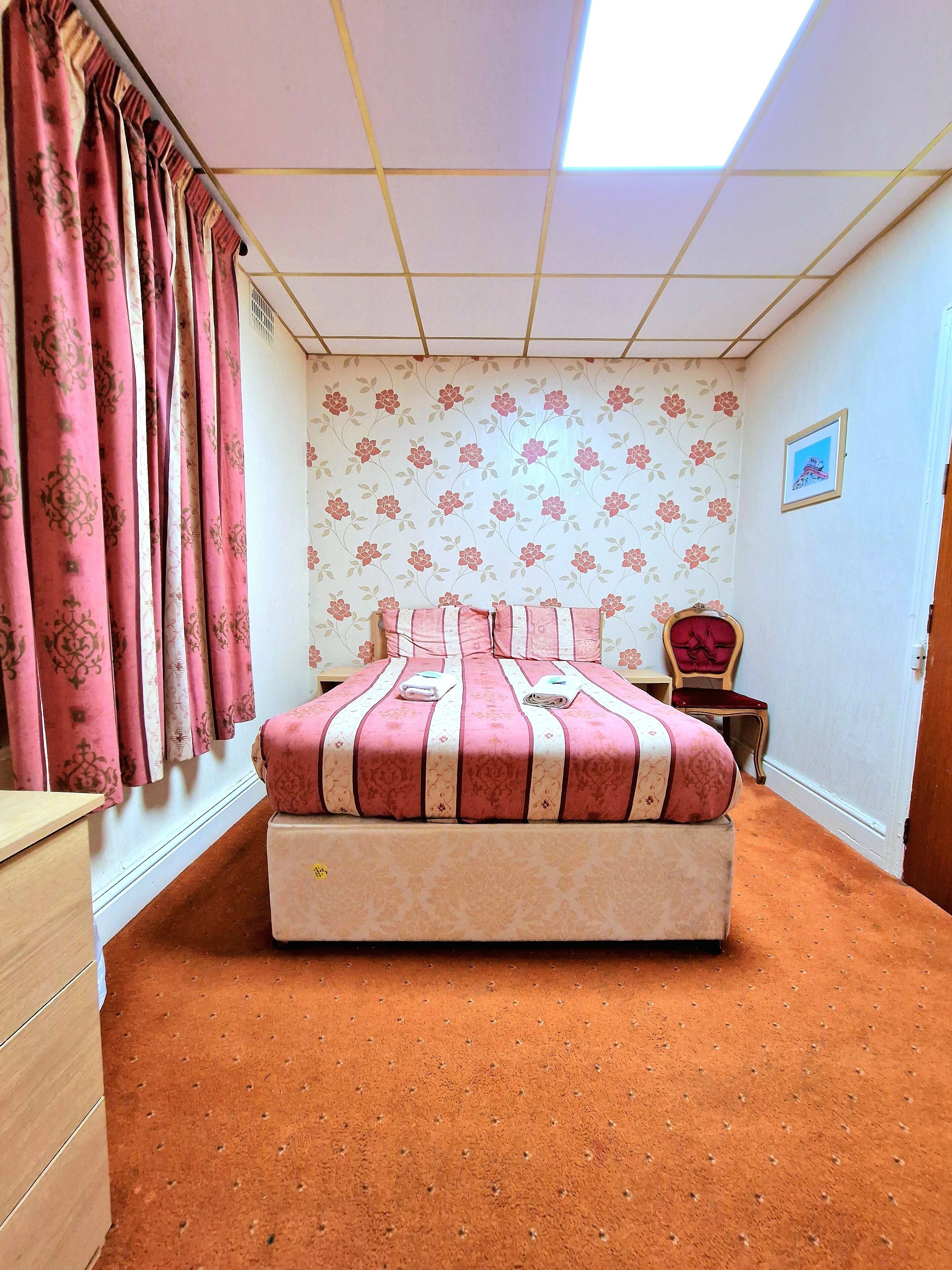A bedroom with a bed, a chair, a dresser, and a window with curtains.