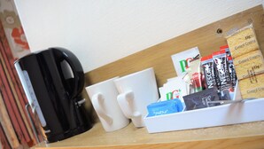 A coffee station with a black coffee maker, white mugs, and a tray with coffee creamer packets. - The Albany Hotel (Blackpool)