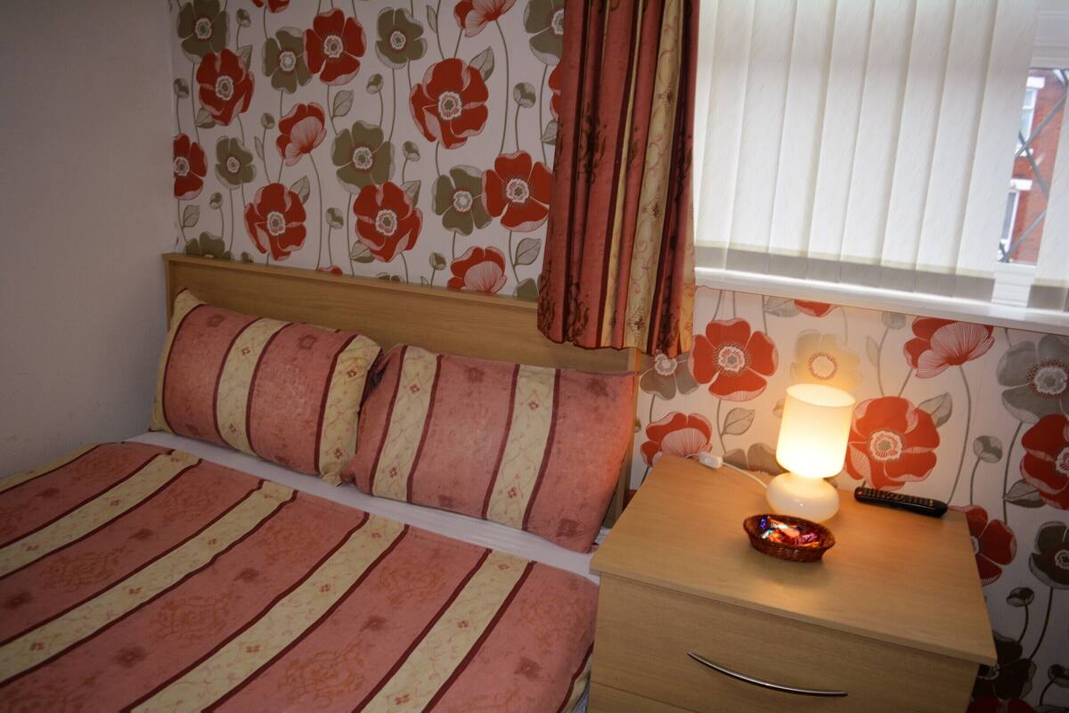 A bedroom with a bed, a bedside table with a lamp, and a window with curtains.