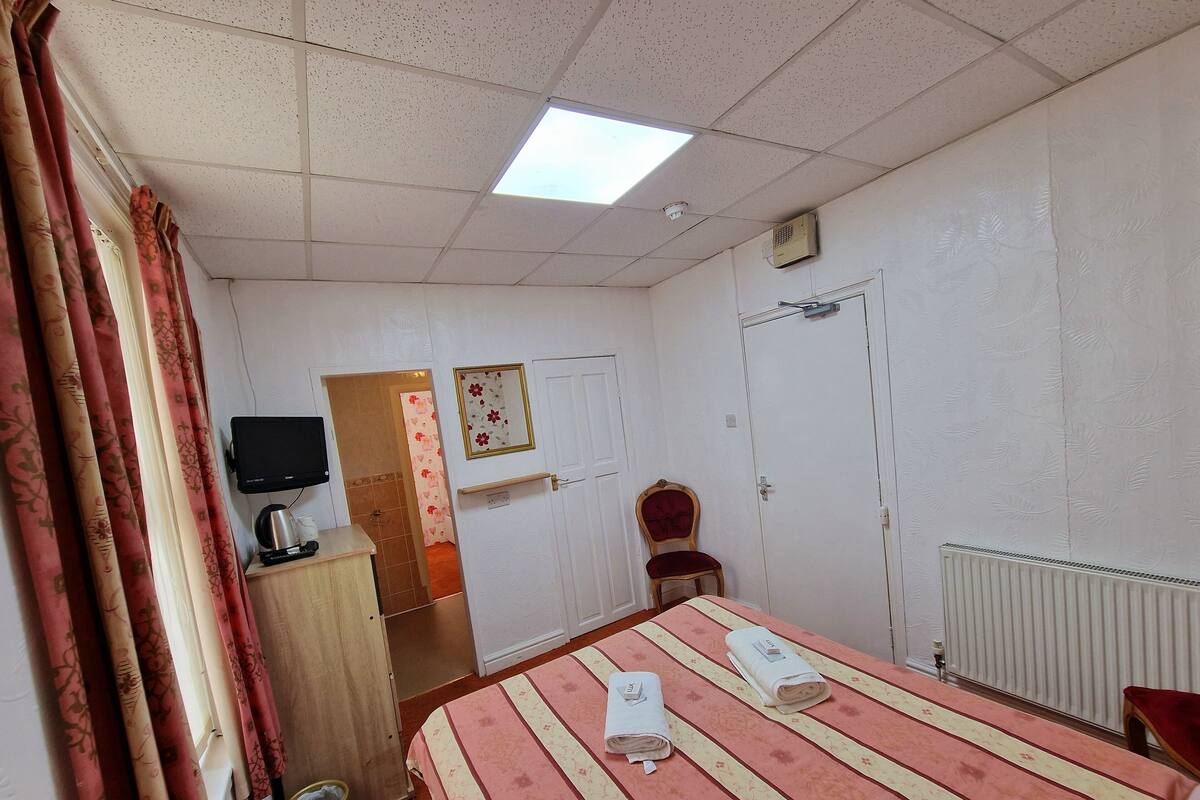 A hotel room with a bed, a desk, a chair, a television, and a radiator.
