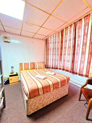 A hotel room with a bed, a nightstand, a chair, a desk, and a window with curtains. - The Albany Hotel (Blackpool)