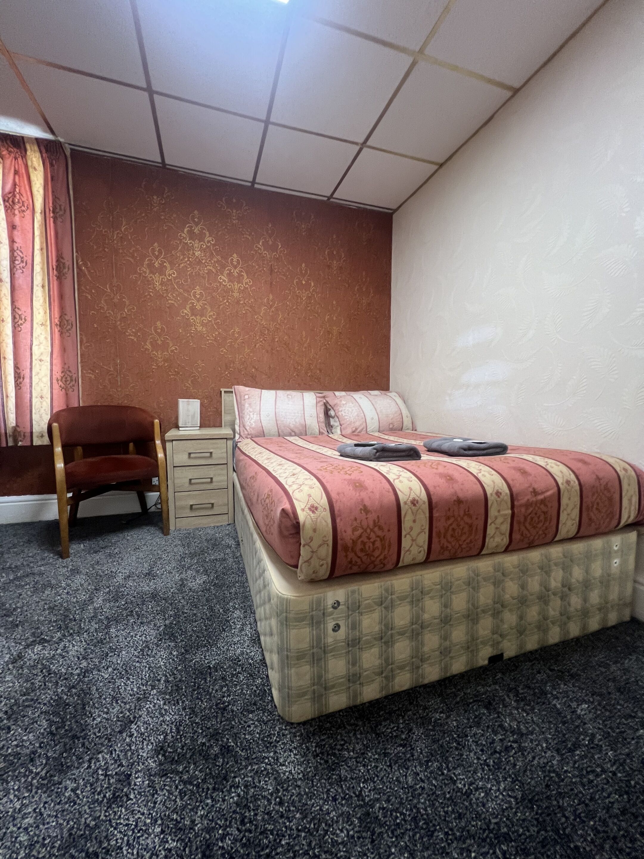 Een hotelkamer met een bed, een stoel, een nachtkastje en een vloerbedekking.