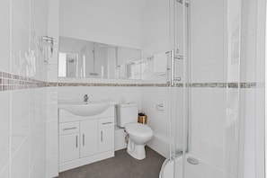 A modern bathroom with a white sink, toilet, and shower. - The Belmont (Torquay)