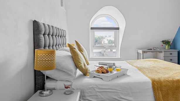 A neatly made bed with a tray of breakfast, a bedside lamp, and a window with a view. - The Belmont (Torquay)