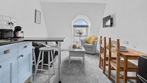 A compact kitchen with a dining area, a small table, and a window with a view. - The Belmont (Torquay)