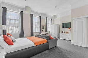 A modern bedroom with a large bed, grey and orange bedding, a desk, and a TV. - The Belmont (Torquay)