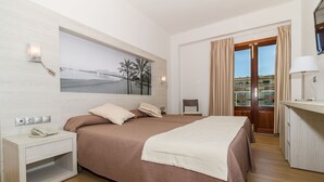 Hotellihuone, jossa on suuri sänky, yöpöytä, jossa on puhelin, rantamaiseman kuvaava taulu ja ovi, josta on näkymä ulos.