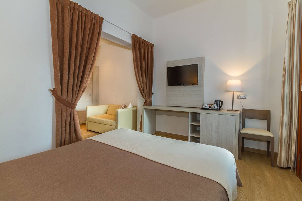 Habitación de hotel con cama, escritorio, televisor, silla y lámpara.