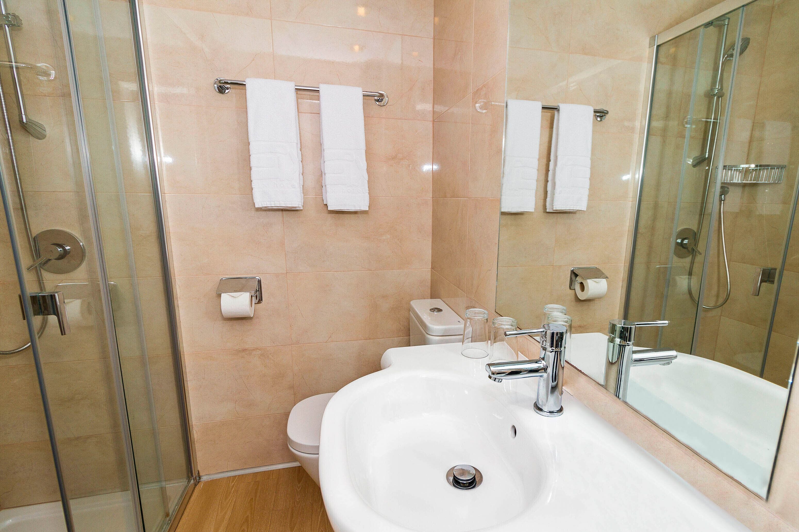 Un baño moderno con ducha de vidrio, lavamanos blanco y grifería cromada, y un espejo grande.
