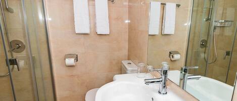 Un baño moderno con ducha de vidrio, lavamanos blanco y grifería cromada, y un espejo grande.
