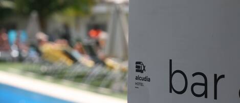 Skilt for Alcudia Hotel med delvis udsigt til en pool og en uskarp baggrund.