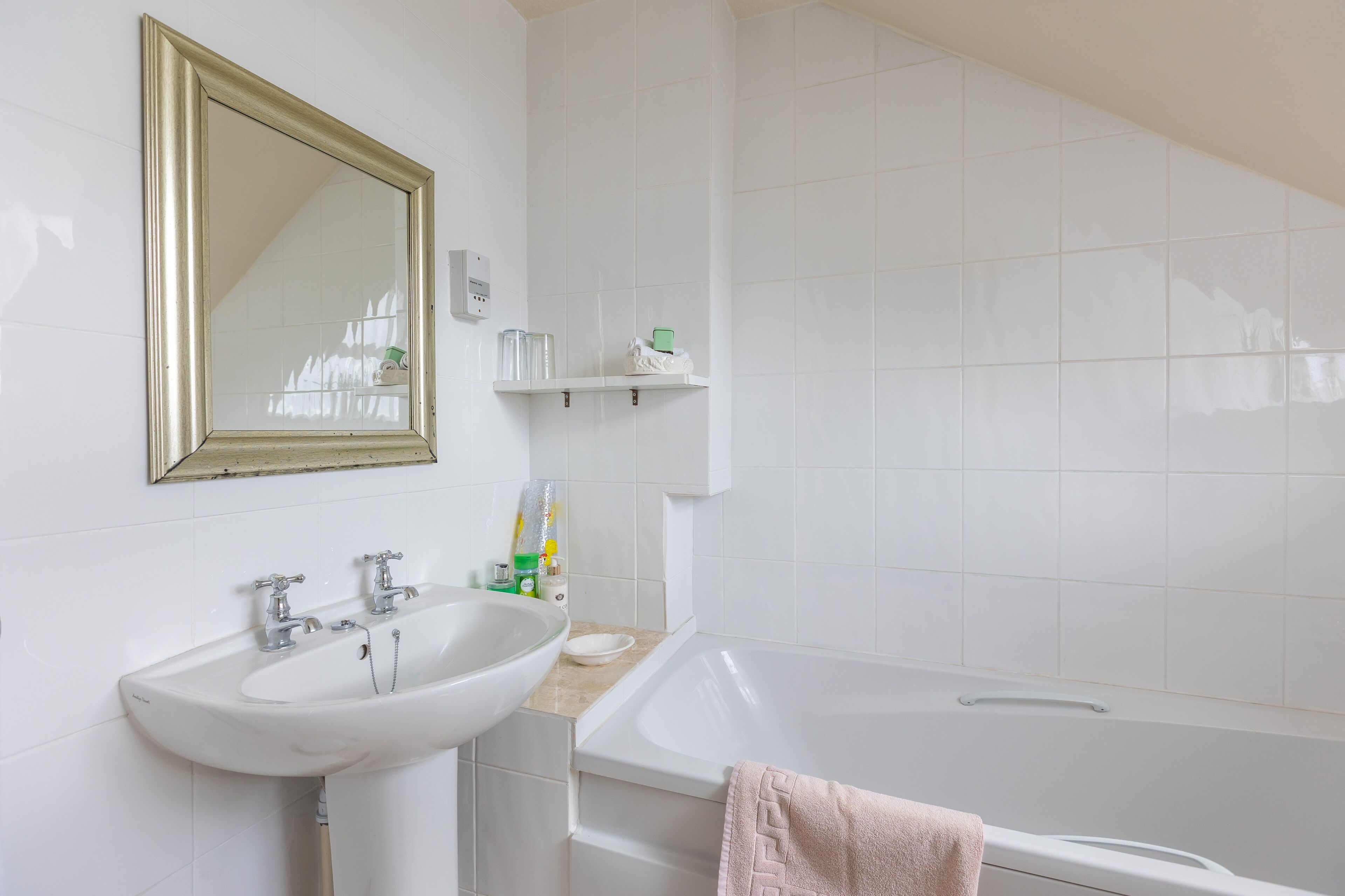 A bathroom with a white sink, a mirror, a bathtub, and a shelf with toiletries.