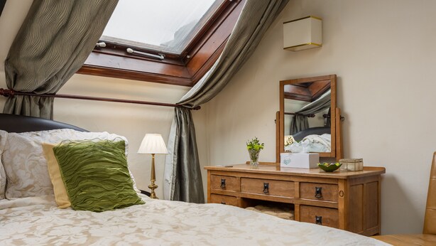Une chambre à coucher avec un grand lit, une commode en bois, un miroir et une lucarne.