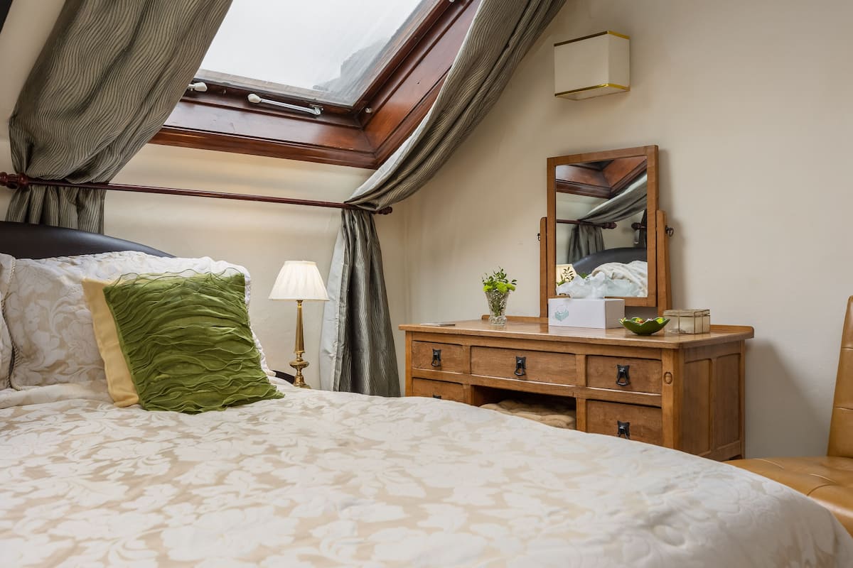 A bedroom with a large bed, a wooden dresser, a mirror, and a skylight.