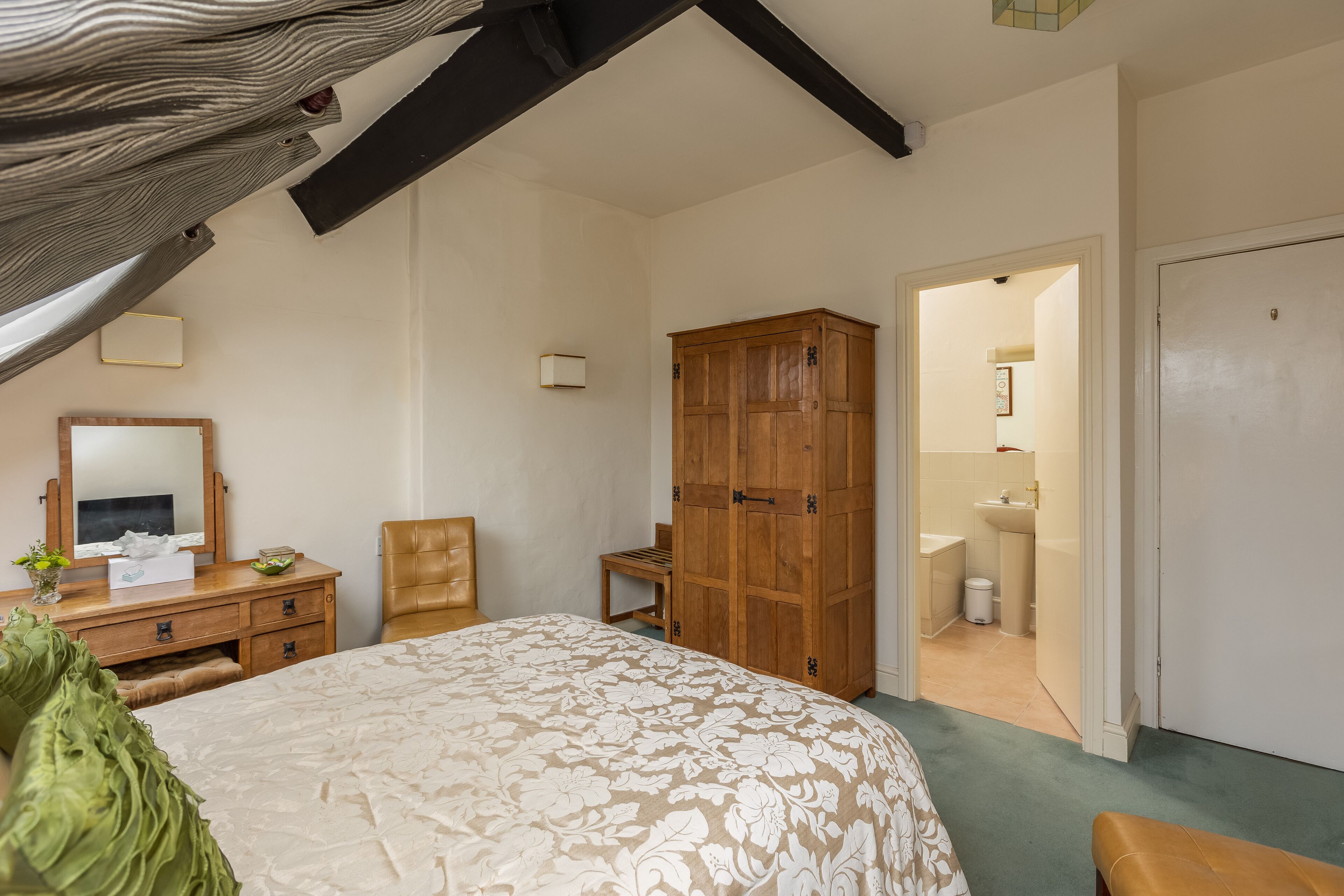 A bedroom with a bed, wooden wardrobe, a desk with a mirror, and a chair.