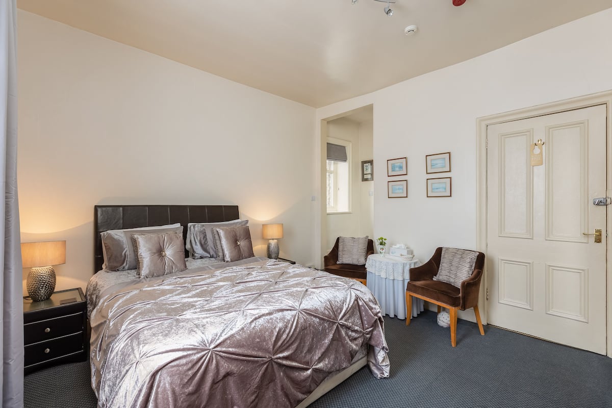 A bedroom with a large bed, bedside tables, a chair, a small table with a lamp, and a door.