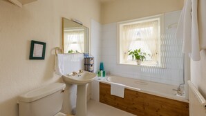 Une salle de bain avec des toilettes, un lavabo et une baignoire. Il y a une fenêtre avec une plante, et une serviette est accrochée au mur.