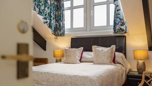 Une chambre à coucher comprenant un lit, deux tables de chevet, une fenêtre avec des rideaux et un luminaire fixé au mur.