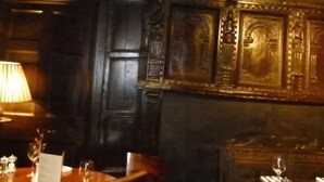 A dimly lit room with a wooden table set for dining, a lamp, and a decorative wall panel. - The Talbot Inn (Ledbury)