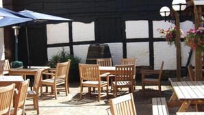 An outdoor patio with wooden tables and chairs, a barbecue grill, and hanging flower baskets. - The Talbot Inn (Ledbury)