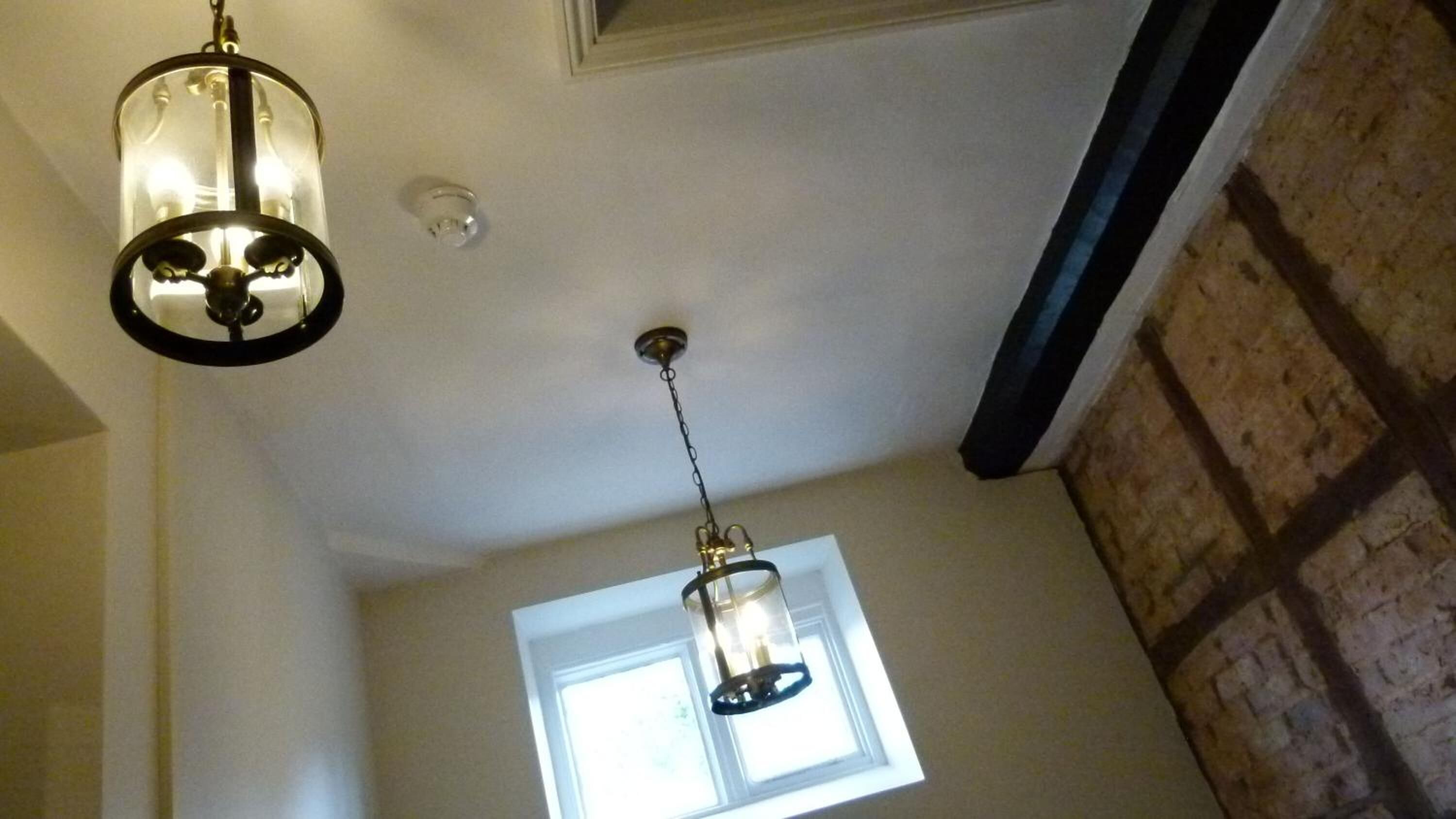 A room with a sloped ceiling, a window with a view, and two hanging light fixtures.