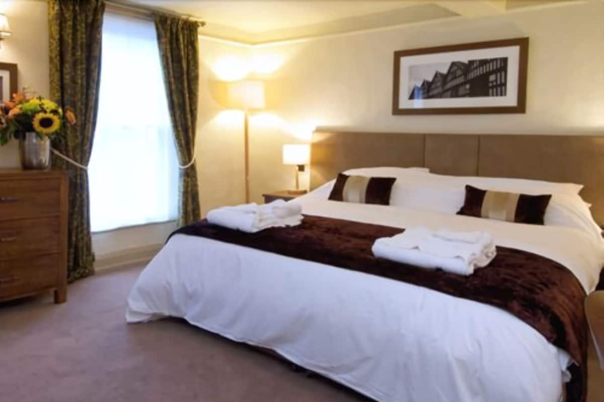 A hotel room with a large bed, a dresser, a lamp, and a framed picture on the wall.
